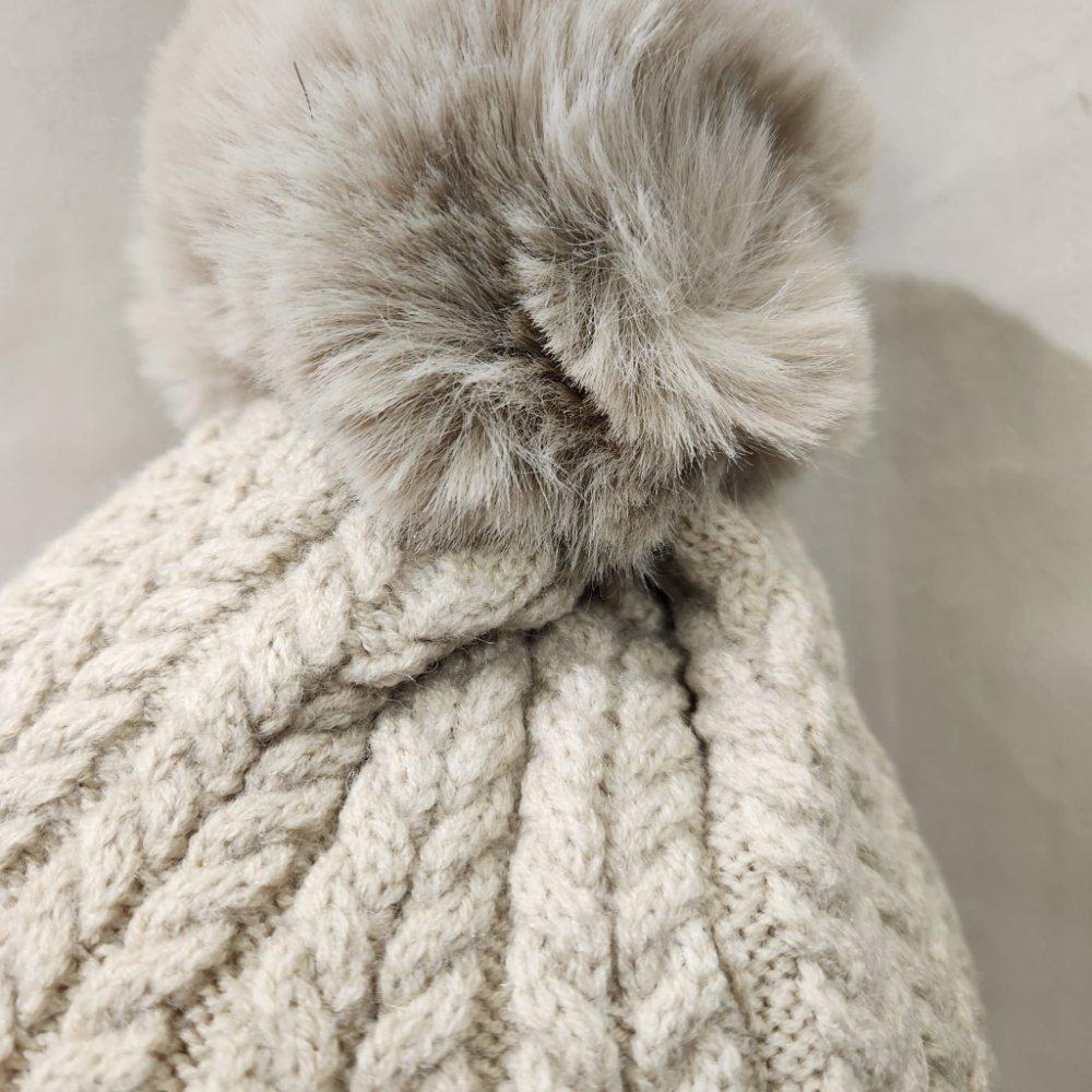 Detailed view of pom pom on light beige beanie