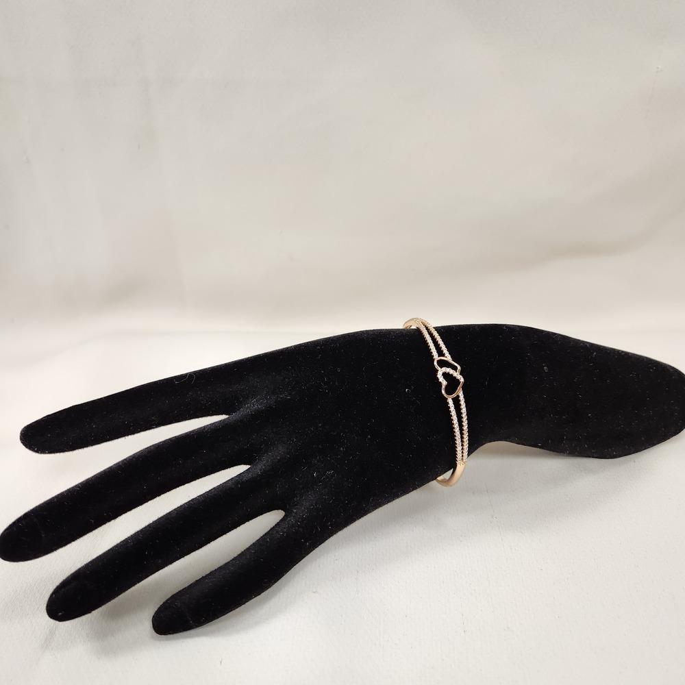 Delicate dual heart gold bracelet displayed on a stand