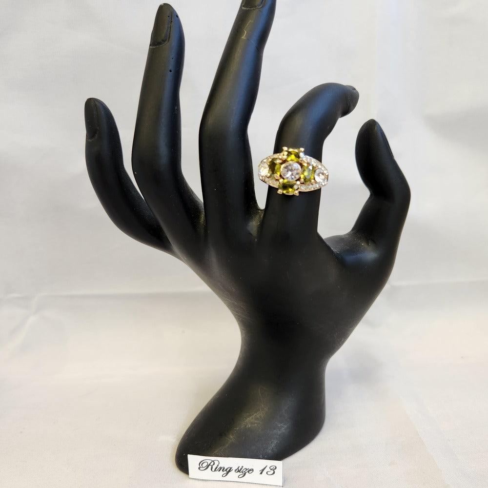 Ring with clear and green colored stones displayed on a mannequin stand