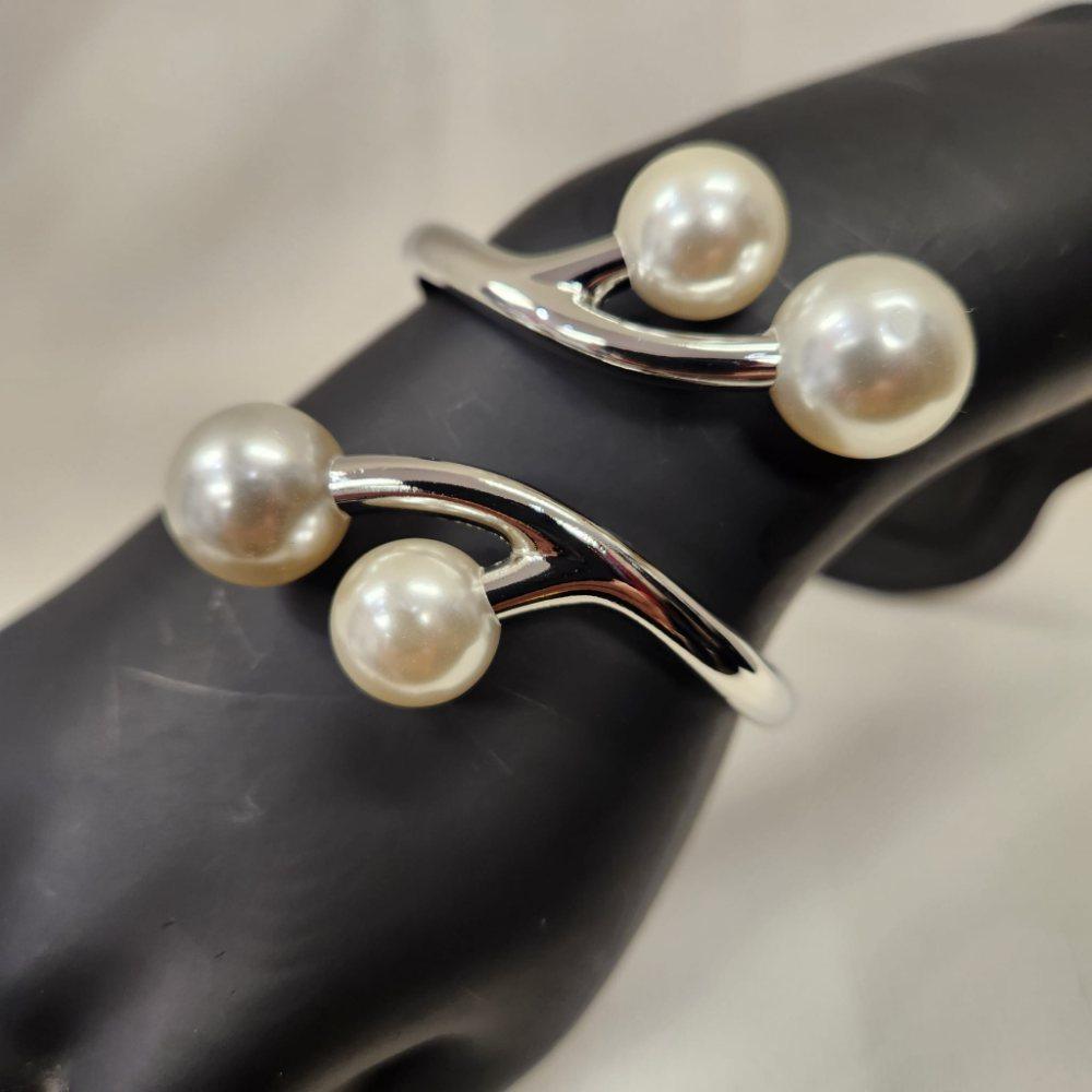 Detailed view of silver hued hinged bracelet with pearl embellishment