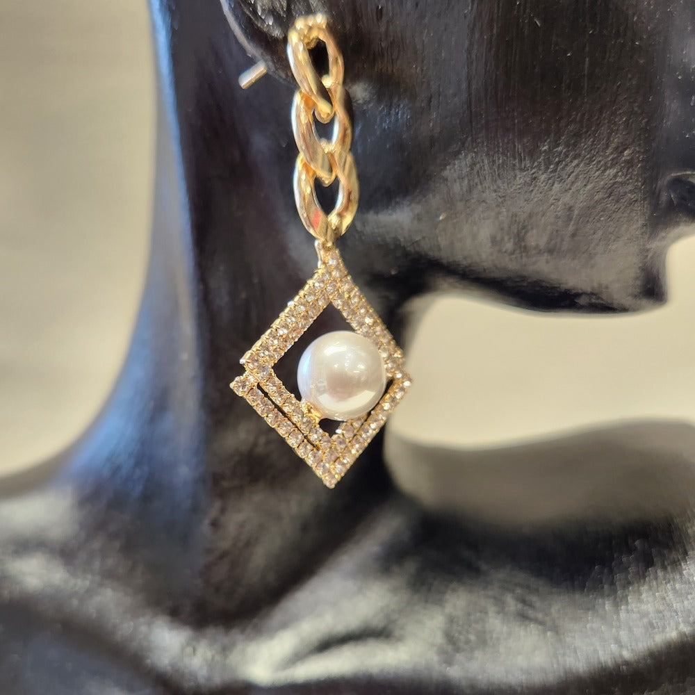 Detailed view of Gold frame dangle earrings with pearl and stone setting 