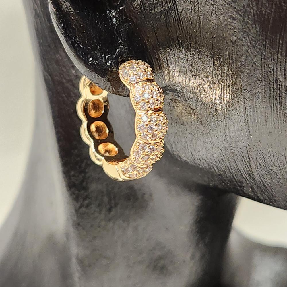 Detailed view of Gold ribbed huggie hoop earrings with stones