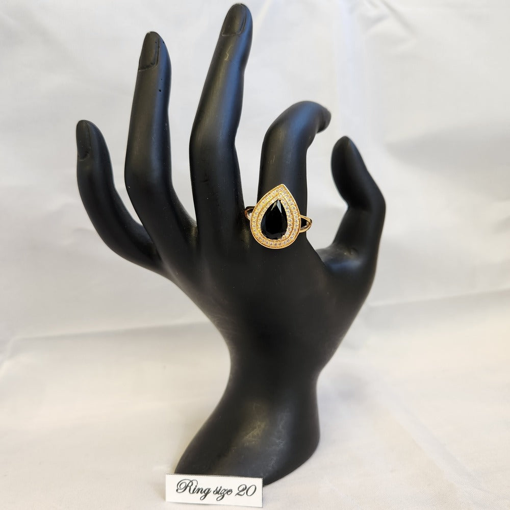 Gold color ring with black pear shaped center stone displayed on a mannequin stand