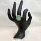 Gold frame ring with oval turquoise center stone displayed on a mannequin stand