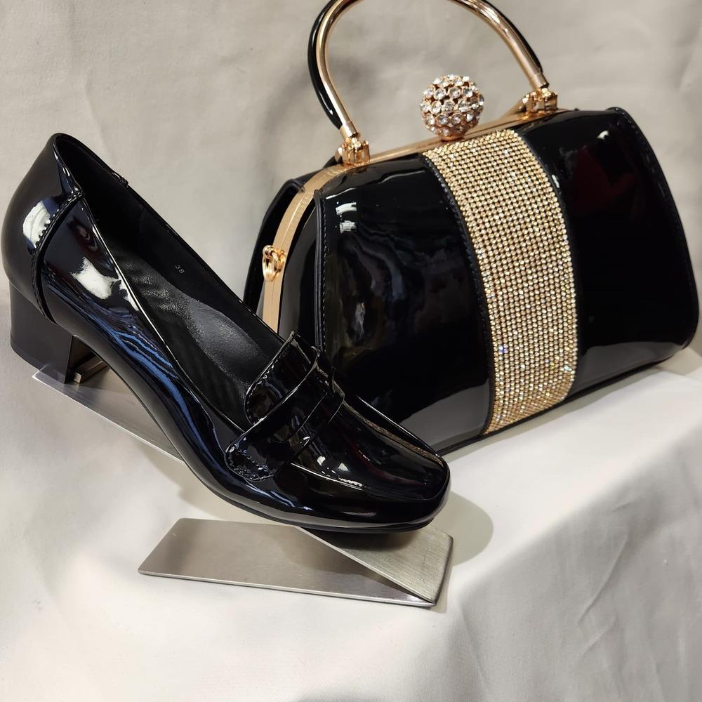 Side view of black patent handbag displayed next to patent black shoe